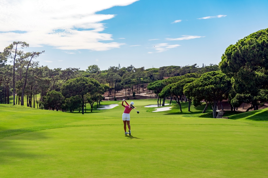 A woman stands on the Quinta do Lago golf course, surrounded by lush green grass and a clear blue sky.