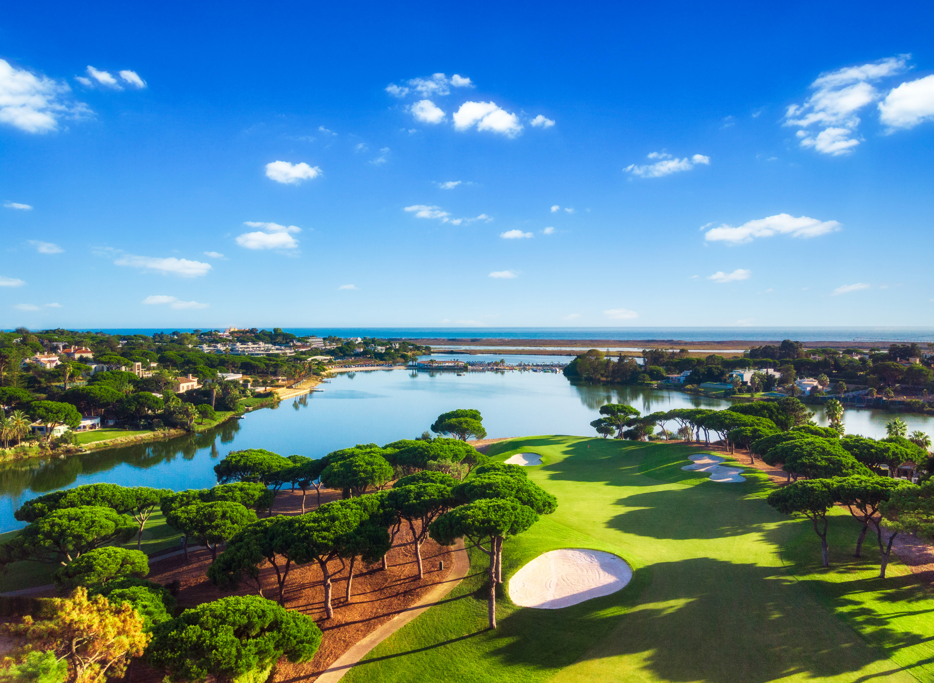 Scenic view of the South Course at Quinta do Lago, with fairways overlooking a tranquil lake and the Algarve coastline. Surrounded by lush greenery and set under a clear blue sky, this iconic championship golf course offers a peaceful, coastal golfing experience in Portugal.
